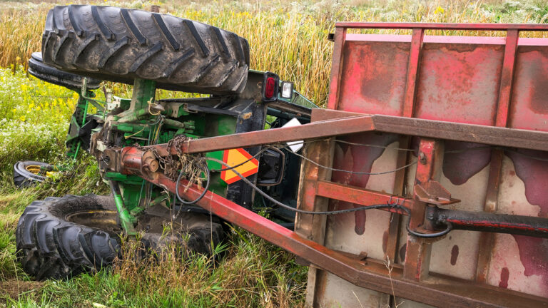A farm tractor and the attached cart lay on their side in a ditc