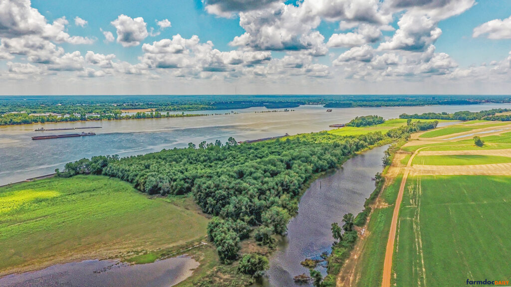 An aerial view captures the bustling barge traffic along the Ohio River, framed by lush agricultural fields and forested banks. Taken near the border of southern Illinois and western Kentucky, the image highlights the intersection of natural landscapes and commercial navigation. (Photo by Jim Baltz)